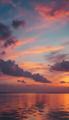 Fototapeta premium A stunning sunset over a calm ocean, with vibrant hues of orange, pink, and purple reflecting on the water's surface. The sky is filled with dramatic clouds, creating a serene and picturesque scene.