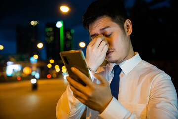 Businessman in frustration rubbing tired eyes after smartphone use in the evening. Serious about...
