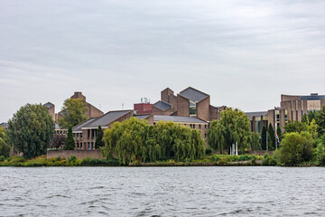 Obraz premium Gouvernement aan de Maas against grey sky, government building on river Meuse surrounded by leafy trees, seen from a boat, cloudy day in Maastricht, South Limburg, Netherlands