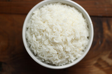 Delicious boiled rice in white bowl, isolated on dark wooden background.  