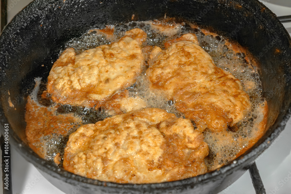 Wall mural schnitzel or chops are fried in boiling oil on an old cast iron hot frying pan. close-up