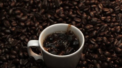 Close up of coffee bean drop in to hot espresso with pile of coffee seed. Macro of freshly roasted bean falling in to cup with aromatic smoke. Slow motion. Organic coffee seed concept. Comestible.