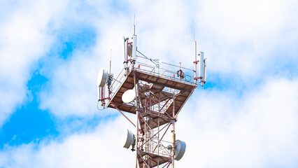A tall tower with a lot of antennas on top. The sky is blue and there are some clouds