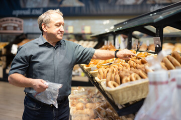 Man takes muffins on shelf of bakery section