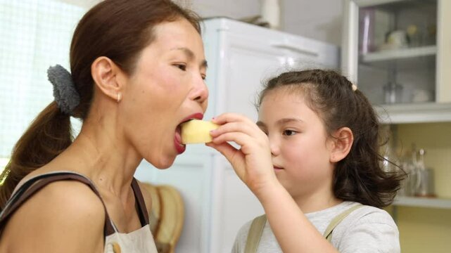 Lively moment of mother and daughter in kitchen, young girl playfully eating bread while laughing and feeding snack to mom. joyful bonding relationship, family lifestyle at home laughter, and fun