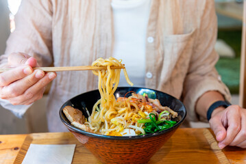 Woman eating a ramen Japanese noodle soup in a black color ramen bowl.