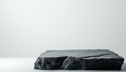 A minimalist black stone slab rests on a smooth surface, contrasting with a plain white wall, showcasing simplicity and elegance.