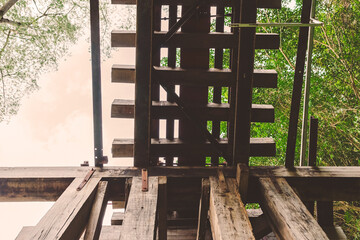The ancient railway piers and large beams made of wood support an old rundown train bridge and were constructed during World War II.  View of old wooden bridge of train railway along cliffs and rivers