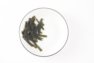 A plate of green seaweed strips sits on a white table