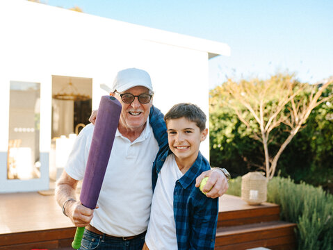 Senior man holding a cricket bat with a young boy outside the house.