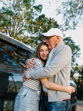 Grandfather embracing granddaughter outside the house.