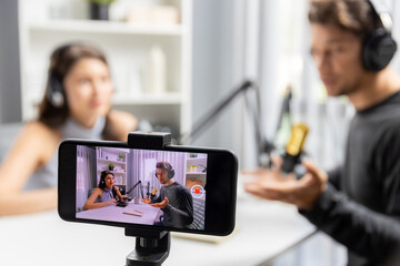Focus on smartphone recording with blurry host channel broadcasters background making advice problem in live streaming with listeners with set live on talking show radio at modern studio. Postulate.