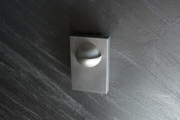 A sleek minimalist motion sensor mounted on a dark wall