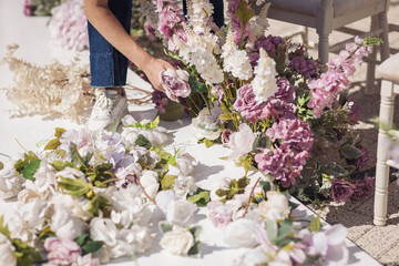 Florist making decorations and arrangements. Woman florist on wedding makes flower composition for wedding from roses, tulips, peonies, orchids to arch. Decorators working at event: birthday, party.