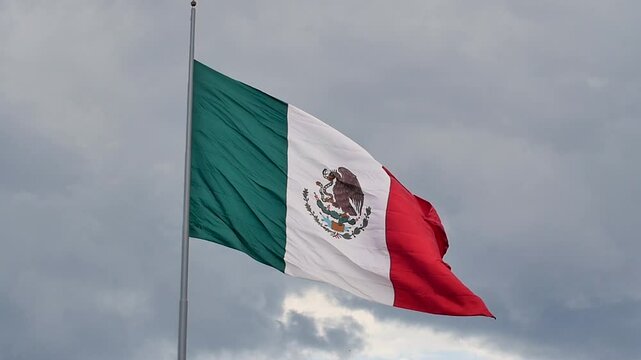 Mexican flag waving against a cloudy blue sky in Mexico