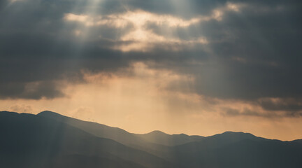 In front of the mountain, the sun shines through the clouds.