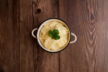 Freshly made bowl of mashed potatoes on a brown wooden table, top down view capturing the creamy texture and simplicity of homemade comfort food