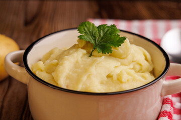 Top View of Mashed Potatoes in a Bowl with Potatoes, Spoon, and Red Napkin on Wooden Table