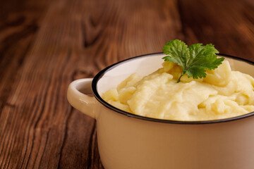 Detailed view of a bowl of fresh mashed potatoes on a rustic brown wooden table, highlighting the creamy texture and warmth of a homemade dish
