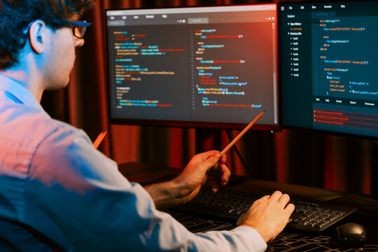 Working IT developer pointing with pencil on online software development coding database application on pc screens, creating program for firmware on website at neon light modern office home. Gusher.