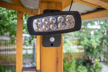 Close-up of an LED spotlight, a spotlight on a wooden post of an open veranda, on a blurred background of the garden. A lantern for lighting the house territory at night
