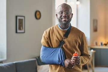 Waist up portrait of smiling adult African American man with broken arm in sling looking at camera...