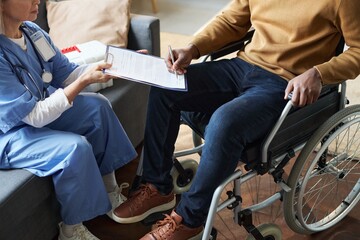 Cropped shot of African American man with disability using wheelchair and signing medical form...