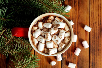  There is a red cup of hot cocoa and marshmallows on a wooden table.
