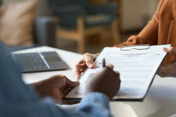 Close up of unrecognizable woman signing tax declaration on clipboard during consultation with financial advisor copy space