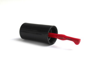 A nail polish brush with red varnish lies on a white background.