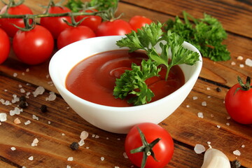 There is a bowl of tomato sauce on the wooden table.