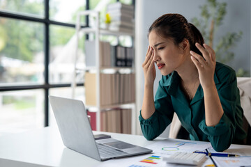 A woman is sitting at a desk with a laptop and a stack of papers