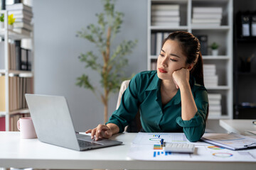 Fototapeta premium A woman is sitting at a desk with a laptop and a stack of papers