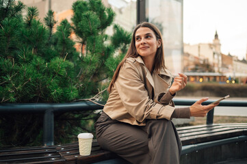 Young businesswoman using smartphone and drinking coffee outdoors