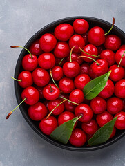 Fresh and vibrant red cherries in black bowl, showcasing their glossy surface and green leaves, perfect for adding burst of color and flavor to any dish