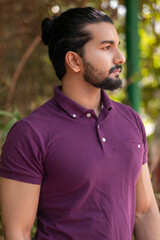 Close-up portrait of a confident, handsome, bearded Asian-Indian man with a ponytail. He's gazing...