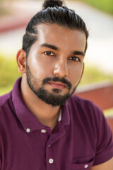 Close-up portrait of a confident, handsome, bearded Asian-Indian man with a ponytail. He faces the camera, showing a range of facial expressions and exuding a calm demeanor.