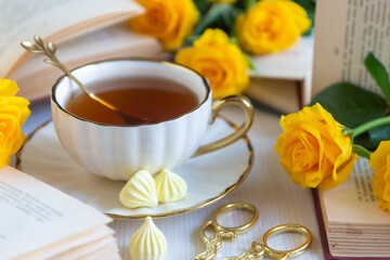 On the white table there is hot tea, cakes and delicate roses.