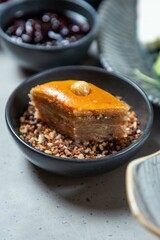 Sweet baklava piece lying on crushed nuts in black bowl