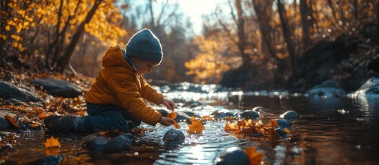 Young child playing with leaves by a stream in the autumn forest.
