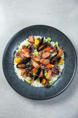 Delicious risotto with grilled seafood and vegetables on gray background