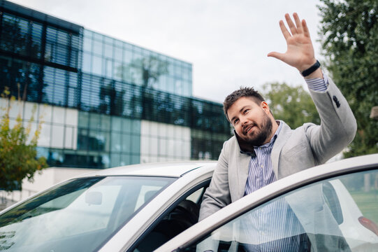 Businessman talking on phone waving from car in front of office building