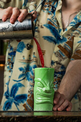 Bartender pouring a cocktail from a shaker into a tiki style glass