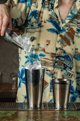 Bartender adding ice cubes into shaker while preparing a cocktail