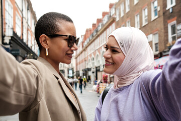 Two female friends doing selfie in the street and looking each other.