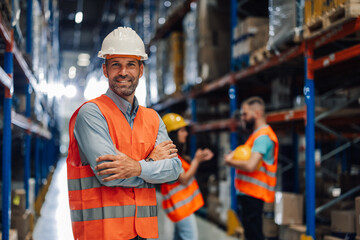 Warehouse manager smiling with crossed arms in busy warehouse