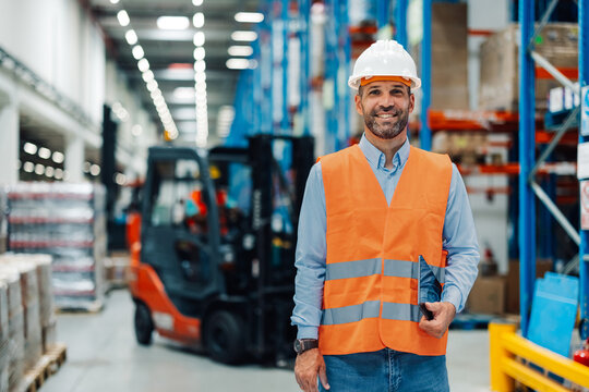 Smiling warehouse worker holding digital tablet with forklift in background