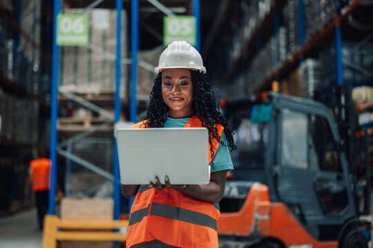 Female warehouse worker using laptop standing in busy warehouse