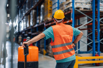 Warehouse worker taking break leaning on pallet truck in warehouse