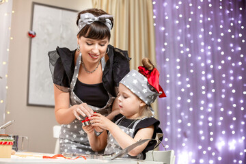  The process of making cookies for Christmas. A young beautiful woman with a girl in gray aprons is preparing dough for making Christmas cookies. Сoncept of mother and daughter. Family concept.